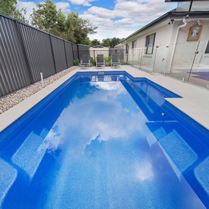 Bright family fibreglass pool reflecting the sky on an open block